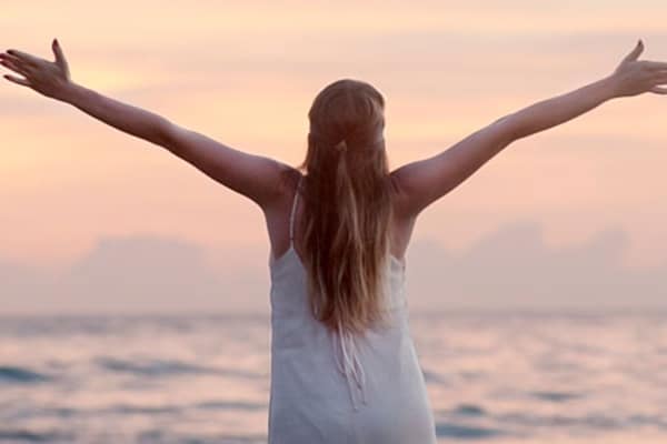 Mujer con los brazos con los extendidos en la orilla de la playa