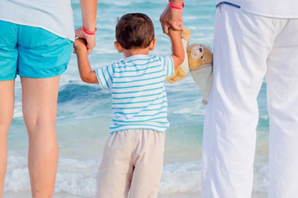 Un niño cogido por sus padres en la orilla de la playa