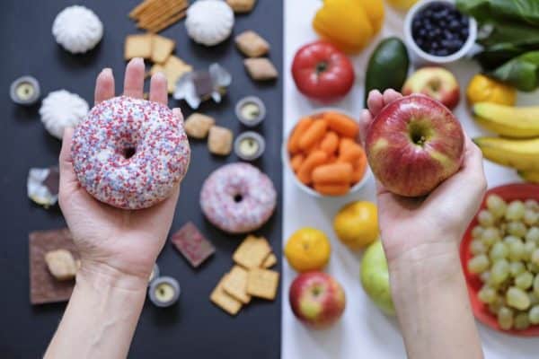 Una mano con un donut frente a otra mano con una manzana