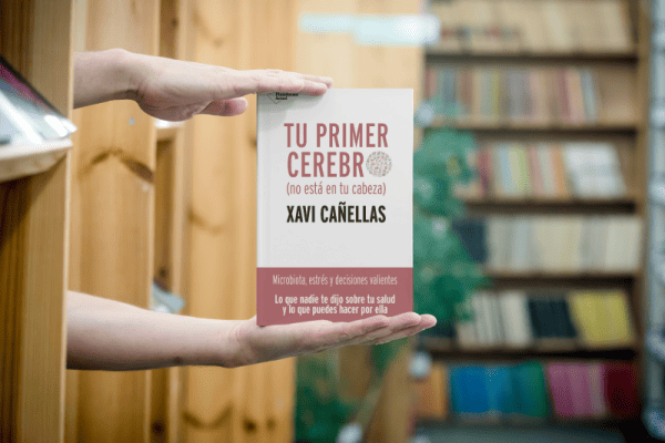 Dos manos sujetando el libro "Tu primer cerebro (no está en tu cabeza)" escrito por Xavi Cañellas